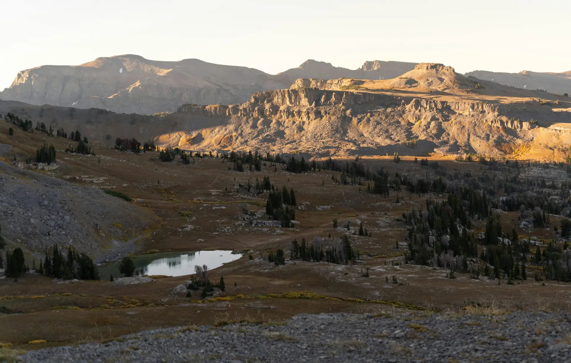 Wyoming mountain landscape with rugged cliffs, alpine meadows, and a peaceful high country lake at sunrise near the Beartooth Mountains
